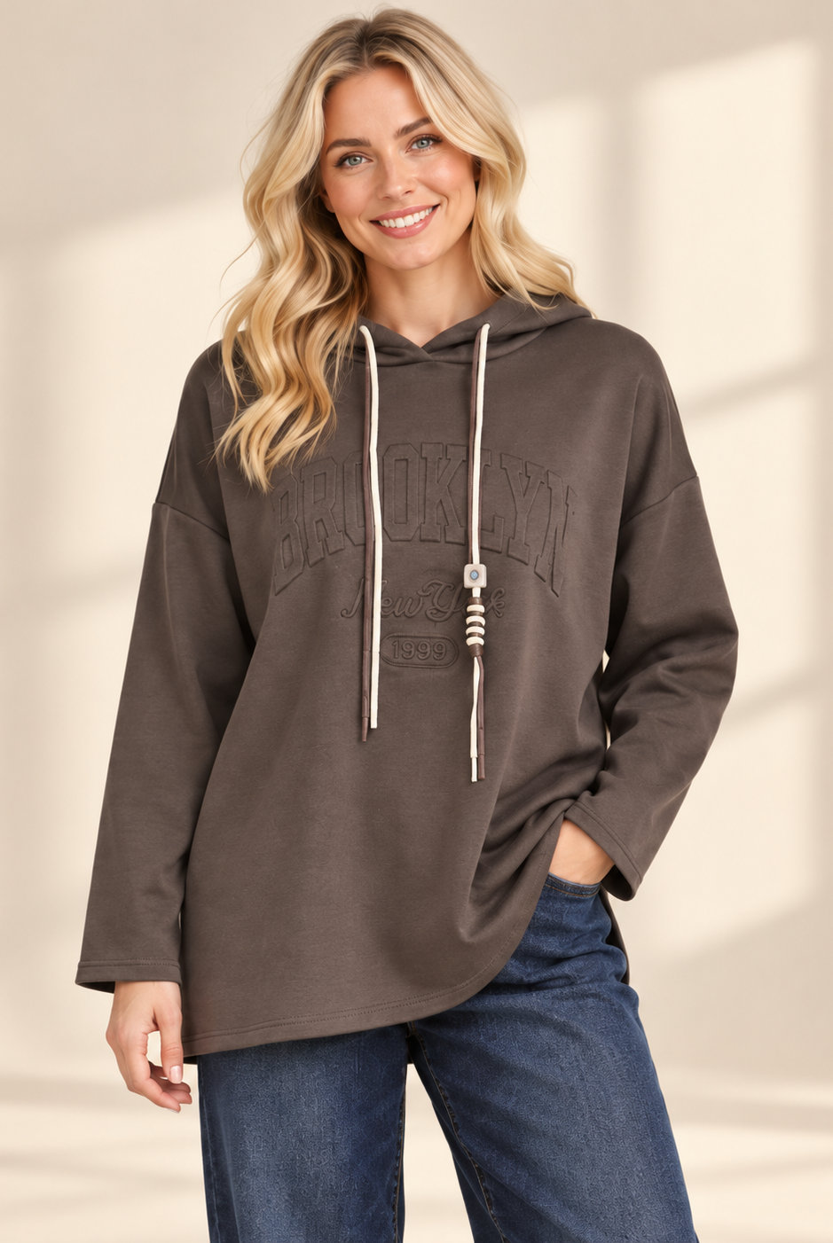 Brun hoodie Brooklyn i längre oversized modell med ton-i-ton-text framtill, huva, kontrasterande dragsnören och långa ärmar med nedhasad axel