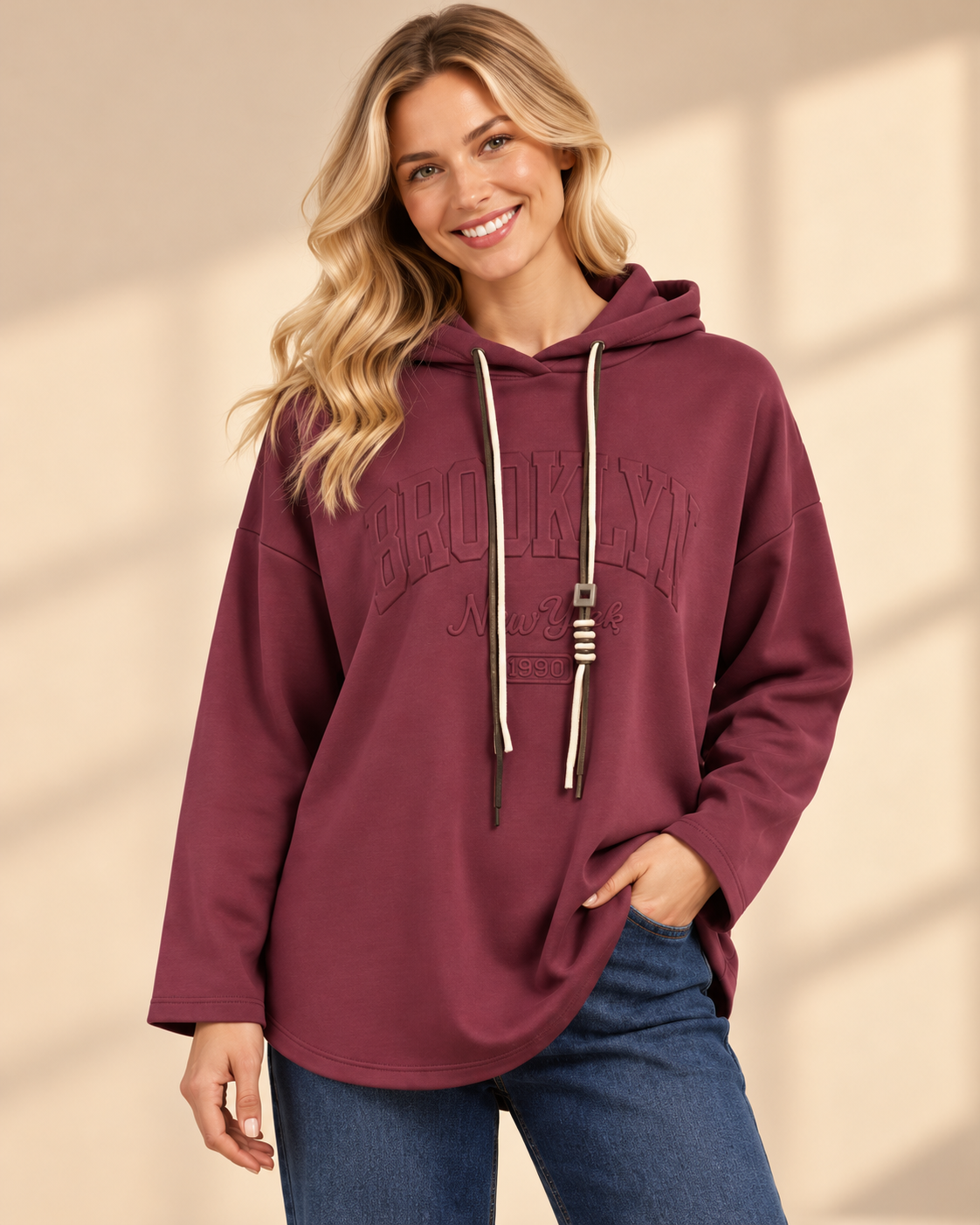 Vinröd hoodie Brooklyn i längre oversized modell med ton-i-ton-text framtill, huva, kontrasterande dragsnören och långa ärmar med nedhasad axel.