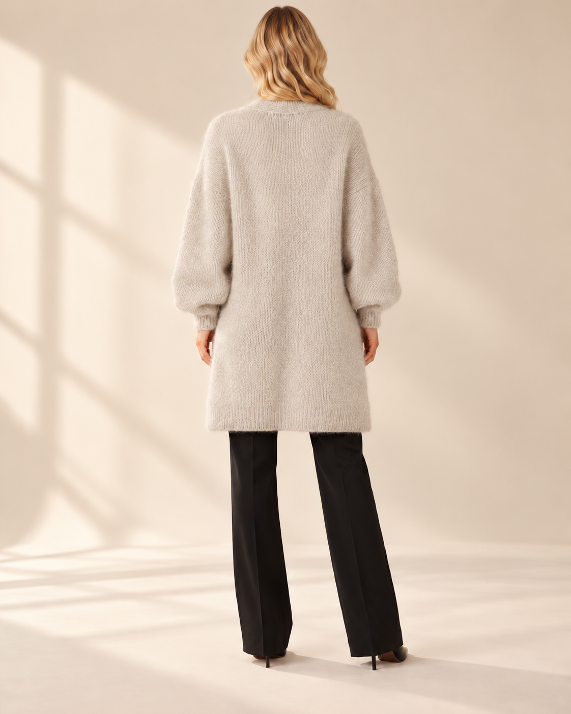 Lång beige mohaircardigan Evelina med luftig stickning, ledig passform och rymliga långa ärmar med ribbstickade muddar, visad på modell.