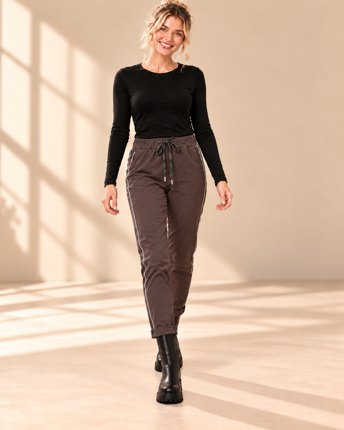 Joggers Diana i brunt med elastisk midja, strassrevär längs sidorna och uppvikta benslut, visade på modell.