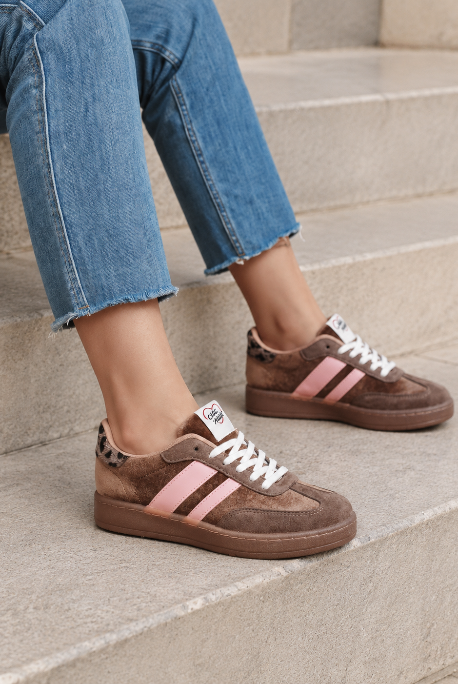 Bruna retro sneakers med rosa detaljer sittande på stentrappa