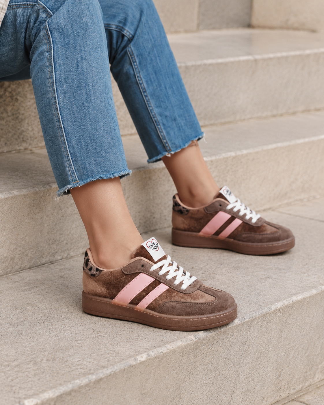 Braune Retro-Sneaker mit rosa Details sitzen auf Steinstufen