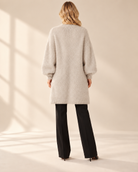 Lång beige mohaircardigan Evelina med luftig stickning, ledig passform och rymliga långa ärmar med ribbstickade muddar, visad på modell.