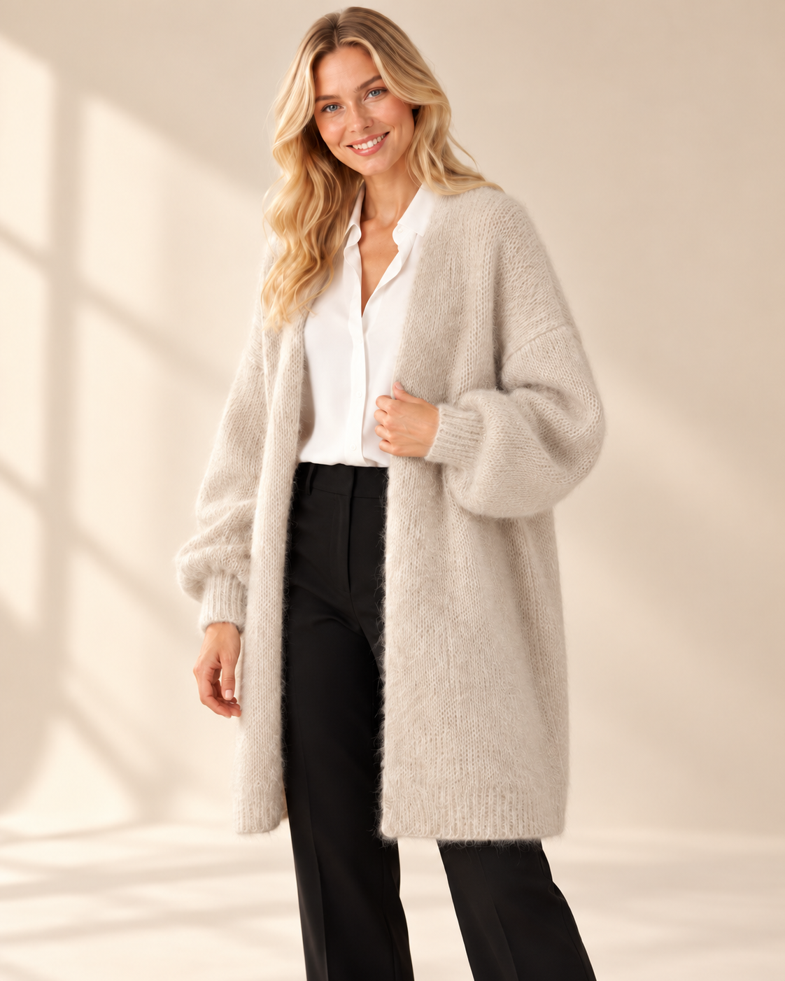 Lång beige mohaircardigan Evelina med luftig stickning, ledig passform och rymliga långa ärmar med ribbstickade muddar, visad på modell.