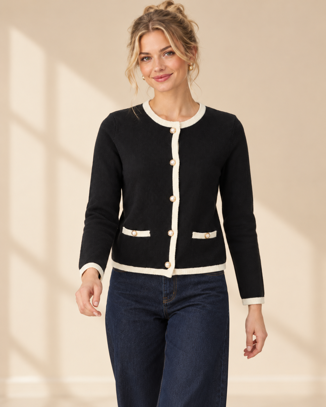 Svart finstickad cardigan Nicolina med offwhite kontrastkanter, rund halsringning, guldfärgade knappar och två fickdetaljer framtill.⠋