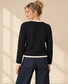 Svart finstickad cardigan Nicolina med offwhite kontrastkanter, rund halsringning, guldfärgade knappar och två fickdetaljer framtill.