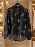 Svart, lätt transparent blus Lollo Gepard med ljusa kattdjursmotiv, långa ärmar med manschetter och rundad nederkant.