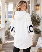Vit hoodiejacka LOVE med grovstickade ärmar, mörk bokstavsdekor, huva med svarta textband, dragkedja och stora framfickor, visad på modell.