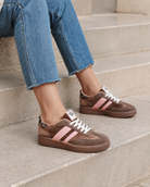 Braune Retro-Sneaker mit rosa Details sitzen auf Steinstufen